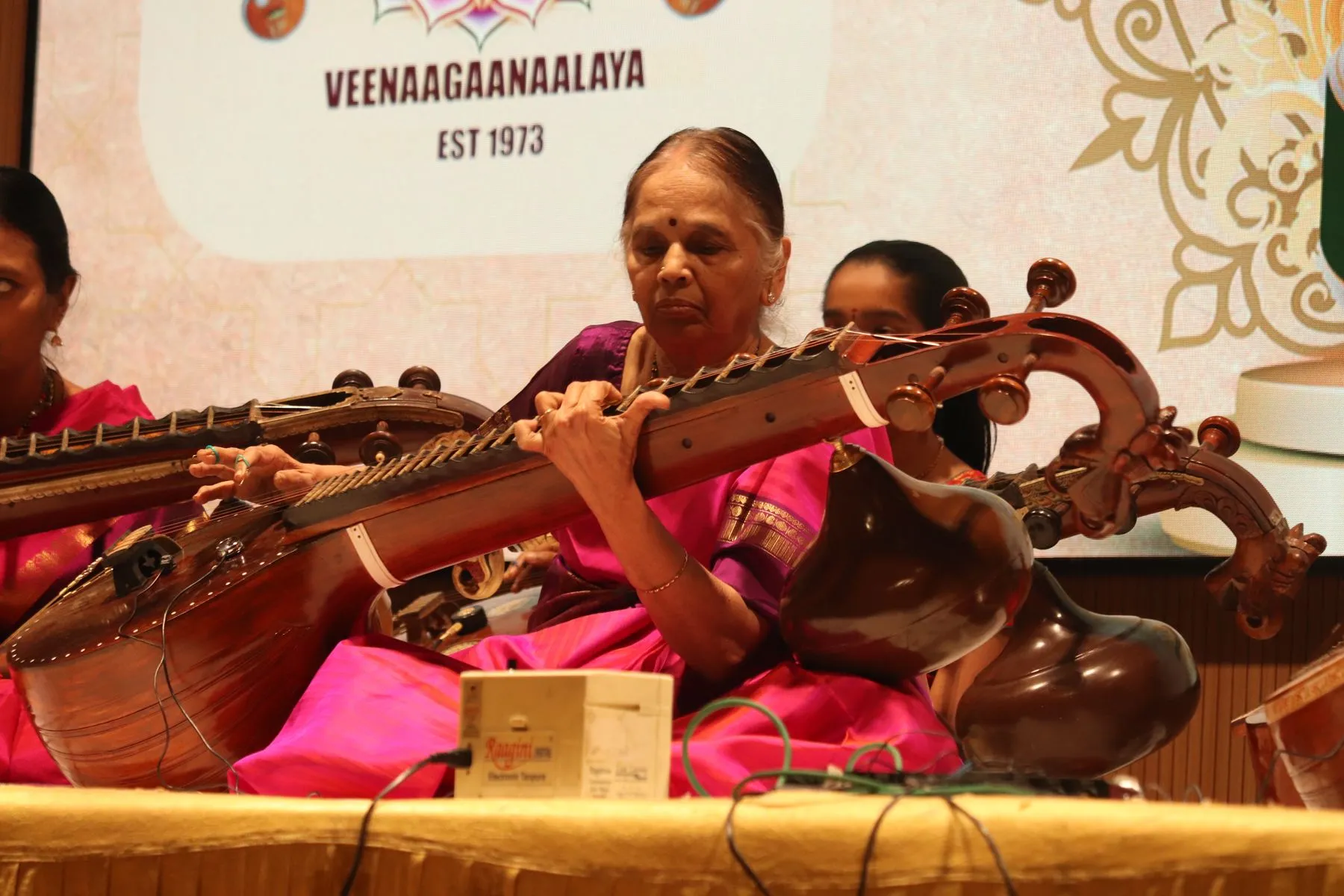 Senior woman vainika with students, Veenagaanalaya backdrop