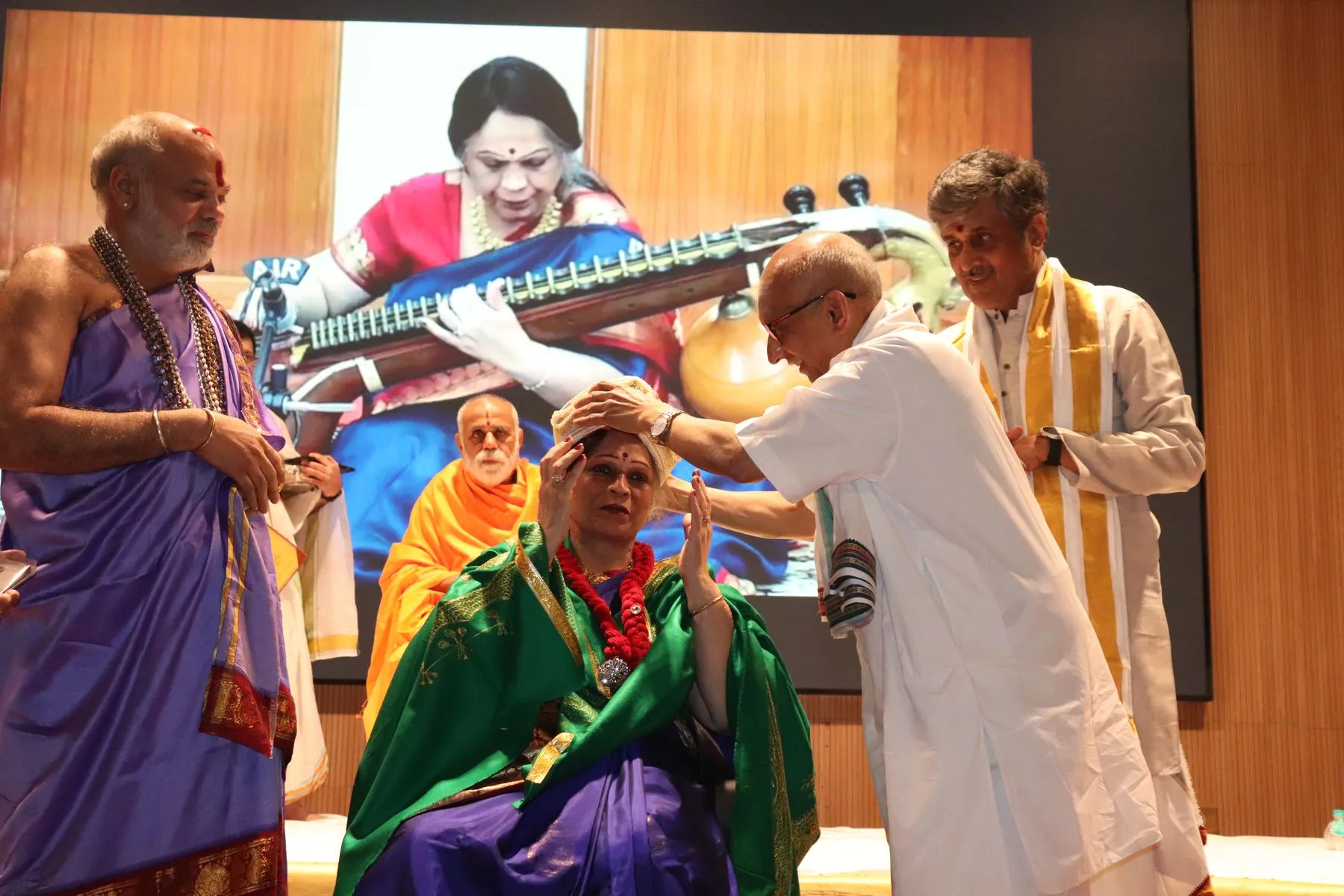 Honoree in namaste under archival veena projection